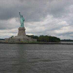 The Statue of Liberty on Liberty Island in New York Harbor, with cloudy skies and surrounding water in the foreground.